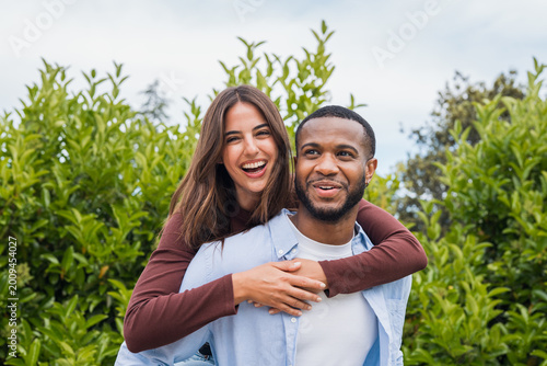 Konstfotografi A joyful young couple share a playful piggyback embrace outdoors, laughing together among green foliage