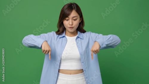Young woman pointing down with both hands on green screen