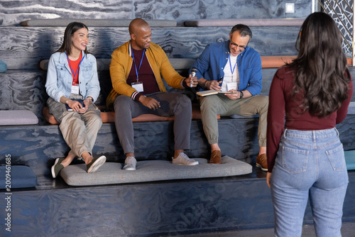 Diverse coworkers interacting with standing presenter at workshop while taking notes with notebook