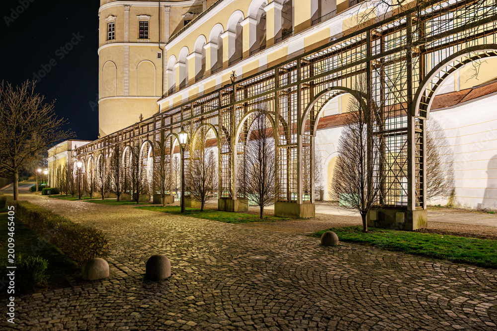 Fototapeta premium Illuminated architectural colonnade at night with trees and arched windows