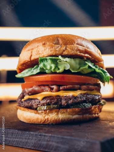 Juicy cheeseburger with bacon, lettuce, tomato, and pickles on a toasted bun, served on a dark surface with a vibrant red background.
