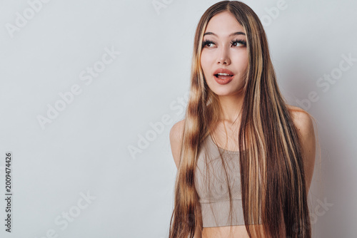 Schilderij op canvas Young woman with long braided hair wearing a sleeveless top standing against a light background looking sideways with a thoughtful expression