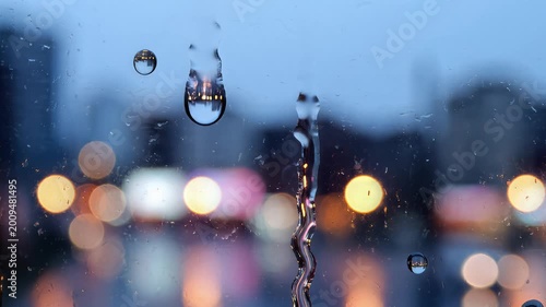 Raindrops sliding down a window with blurry city lights at night