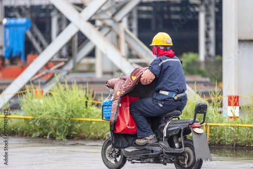 Schilderij op canvas Worker riding scooter across a shipyard yard in the rain, end of workday in heavy industry environment