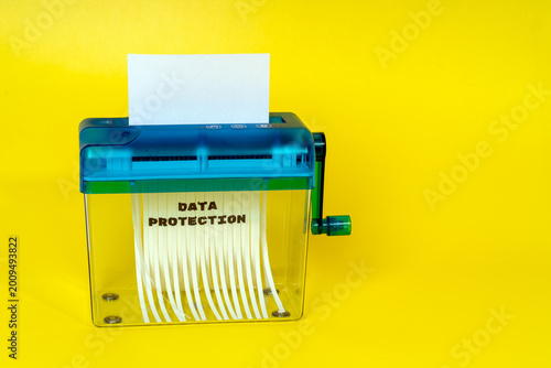 Paper shredder shredding confidential document for data protection concept on yellow background