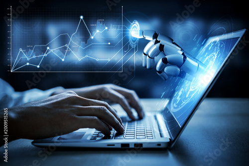 Fotografi A human hand types on a laptop while a robotic hand interacts with digital data displayed on the screen