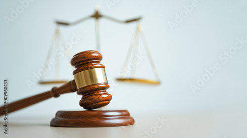Wooden judge gavel with justice scales in background, symbolizing legal authority, court decisions, fairness, law enforcement and professional judicial system concepts.