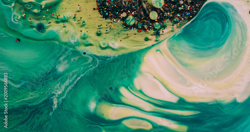 Liquid glitter flow. Ink wave. Defocused green yellow color shiny sequin bright particles oil bubbles floating in water on abstract background.