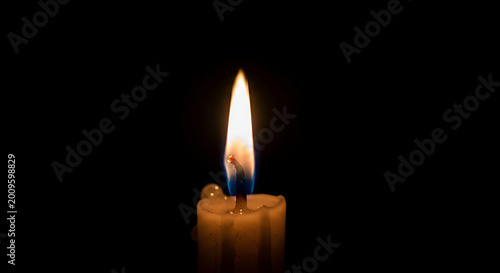 Close up of a lit candle with a bright flame against a black background showing melting wax