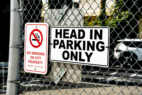 Schilderij op canvas No Smoking and Head In Parking Only signs on a chain link fence
