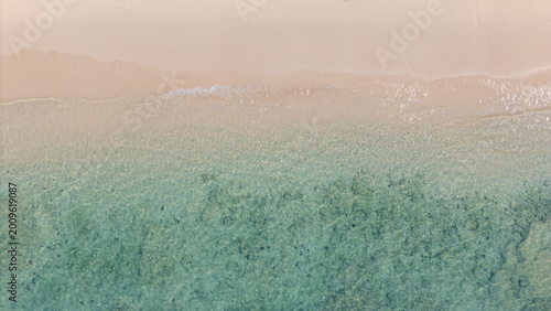 A serene beach scene showing gentle waves washing onto smooth sand, blending soft beige and turquoise hues in a tranquil coastal setting.