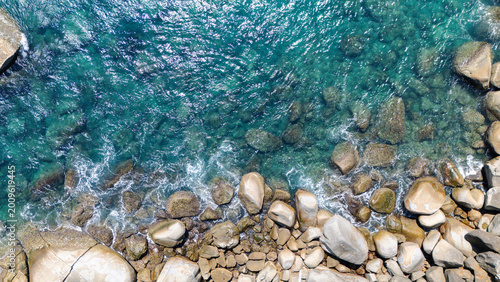 Clear turquoise water flows over various smooth stones along a rocky shoreline, creating a natural, serene coastal scene.