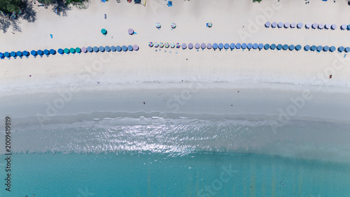 Photography Aerial view of a pristine beach with rows of colorful umbrellas and clear turquoise water gently lapping the shore
