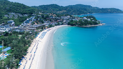 Photos A stunning aerial view of a tropical beach with clear turquoise water, white sand, and a resort town nestled among green hills