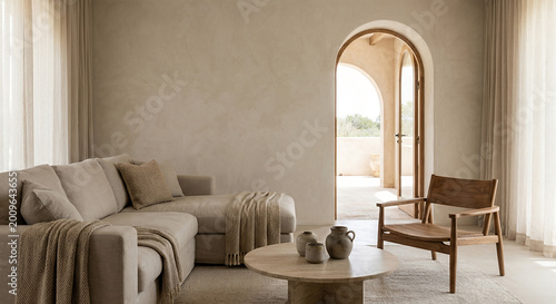A neutral-toned living room with a sectional sofa, a wooden armchair, and a round coffee table with decorative vases, leading to an arched doorway with a view of an outdoor patio.
