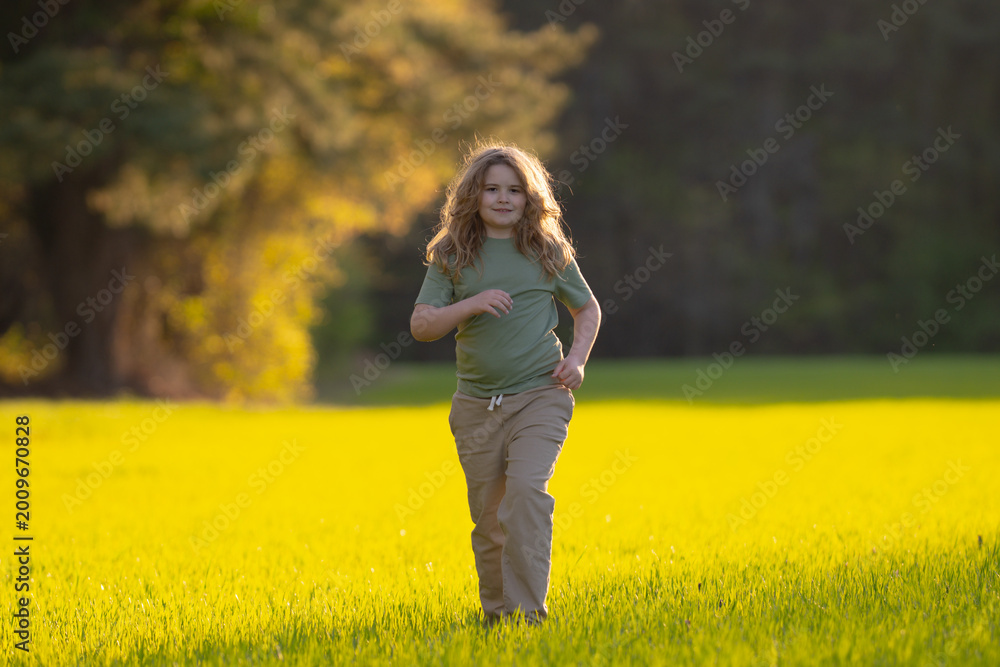 Fototapeta premium Child running in summer field. Happy kid run outdoors. Child on nature. Child in run motion on grass. Kid running at sun light. Teen running in meadow. Portrait of running child.