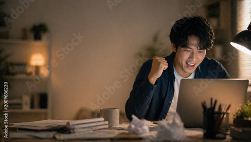 Happy asian man celebrating success at night with laptop