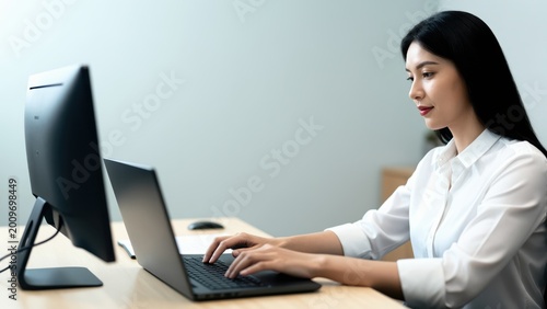 Focused Productivity: A focused professional engrossed in her work, typing diligently on a laptop while the adjacent computer monitor provides additional workspace.
