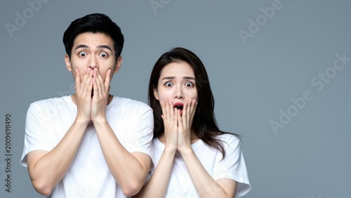 Shocked Couple: A young couple expresses surprise and disbelief, their hands covering their mouths in a moment of astonishment. Capturing the raw emotion of unexpected news or a startling revelation.