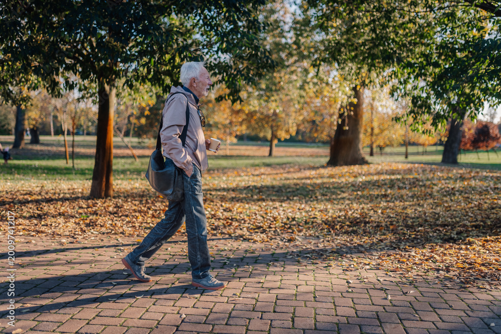 Fototapeta premium Senior man walking with coffee in autumn park