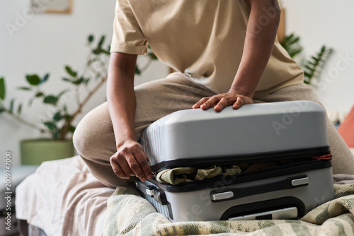 Canvas Print Young adult woman pressing suitcase closed while packing for trip at home, close up