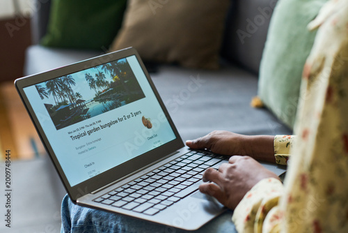 Foto Young adult woman browsing resort booking on laptop while preparing for trip, comparing travel accommodation options
