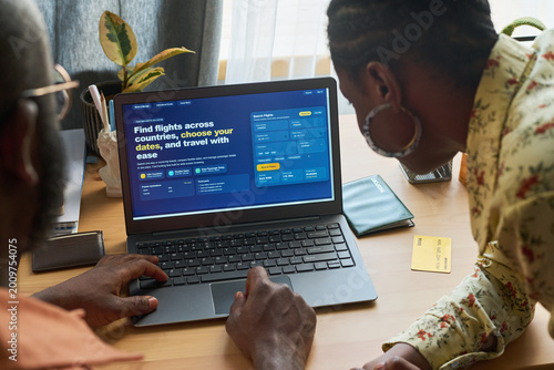 Obraz na plátne Black couple booking flights on laptop while preparing for trip, comparing travel options and payment details