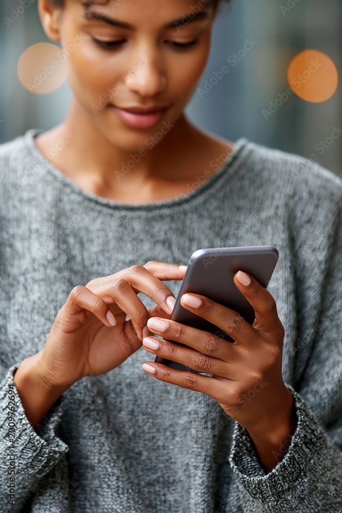 Fototapeta premium Young woman tapping smartphone with cropped hands in city