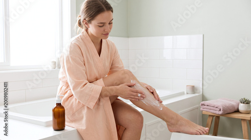  Woman Applying Moisturizing Cream on Legs in Bathroom
