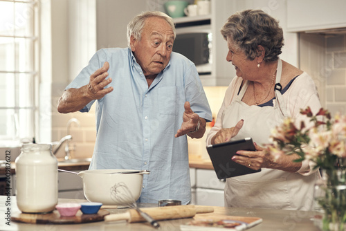 Bild auf Leinwand Confused, old couple and baking with tablet in kitchen for recipe doubt, tutorial error or uncertain