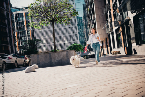 Foto Woman walking a fluffy white dog through a sunny urban plaza with coffee and a p
