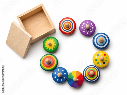 New wooden and colorful spinning tops arranged in a clean flat lay composition with several brightly painted tops displayed in a neat circular pattern and a small open storage box nearby