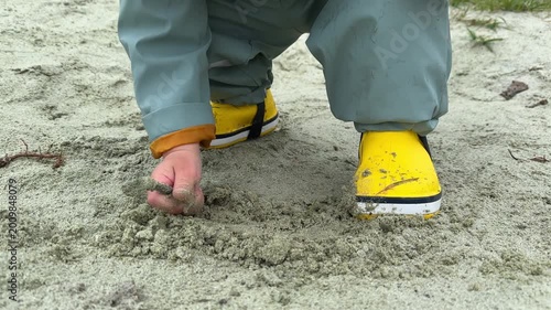 Child digging in sand wearing yellow rain boots