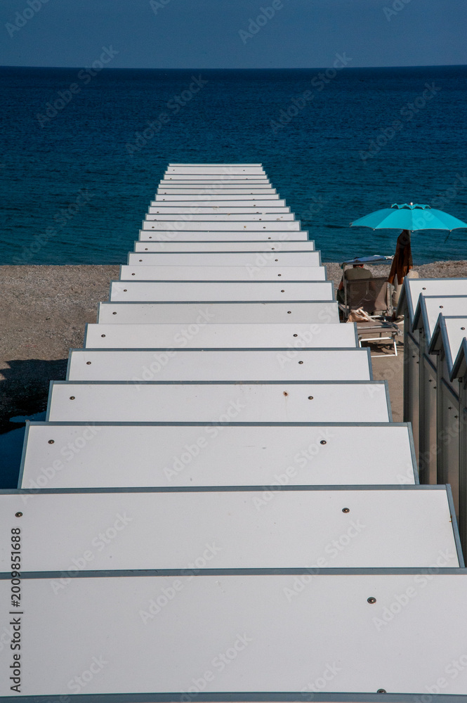 Fototapeta premium Scale bianche che portano al mare con ombrellone blu e lettini