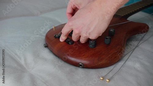 A steady shot of a musician's hand polishing a beautiful wooden bass guitar on a sofa. The scene captures the meticulous process of instrument preservation and the passion for music gear maintenance i