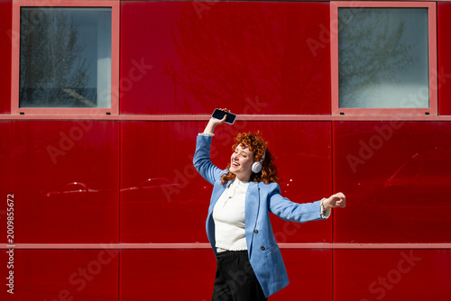Businesswoman dancing outdoors with headphones and smartphone