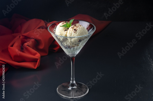 Ice cream with chocolate in a martini glass and mint on a black background. On a dark stone background.