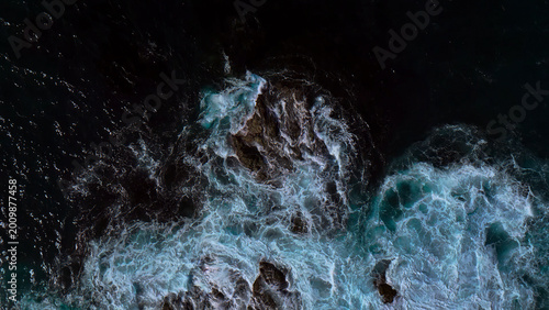 Dramatic aerial view of powerful ocean waves crashing against dark rocks, a dynamic seascape with frothy white and turquoise water, perfect for nature and travel themes.