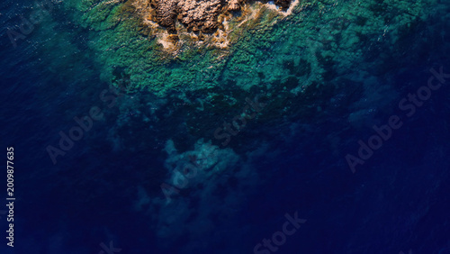Aerial view of a rocky island surrounded by deep blue and turquoise ocean water, a vibrant marine ecosystem, and clear sea for travel and nature concepts.