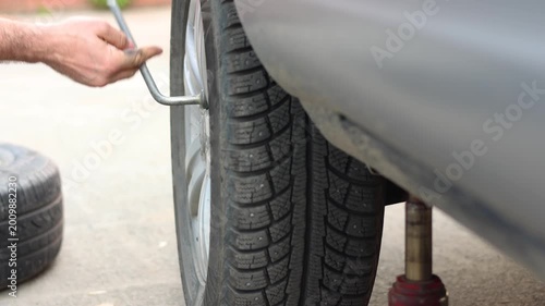 A man loosens a car's lug nuts with a lug wrench to replace or repair them. Close-up of his hands. The car is raised with a hydraulic jack. Slow motion 4k footage.