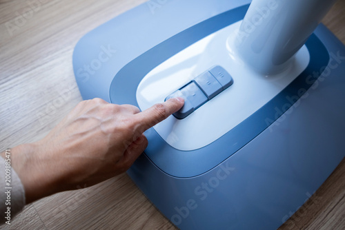 Canvas-taulu Close-up of hand pressing power button on electric fan control panel placed on wooden floor