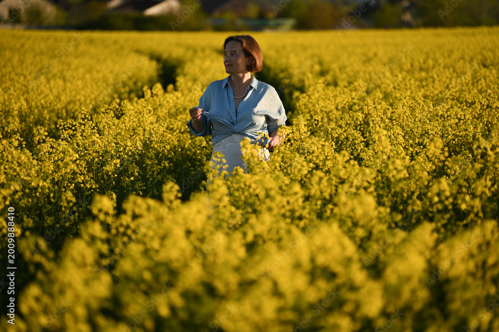 Fototapeta premium Happy smiling woman with hat in yellow rapeseed field at sunset