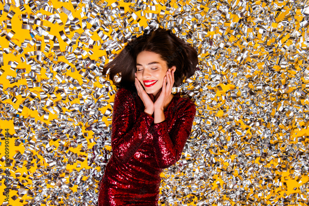 Obraz premium Woman in red sequin dress lying in silver confetti celebrating with joyful smile and festive glamour