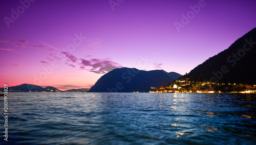 Beleuchteter Küstenort Peschiera Maraglio auf Monte Isola am Iseosee in der Abenddämmerung, Italien