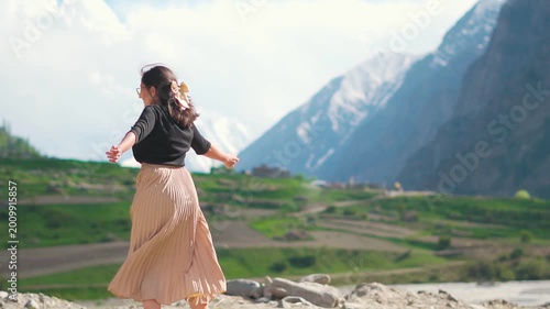 Beautiful Indian girl twirl with joy while standing against Himalaya mountains at Miyar Valley, Lahaul, India. Summertime, mountain escapes, holiday vibes and travel concept.