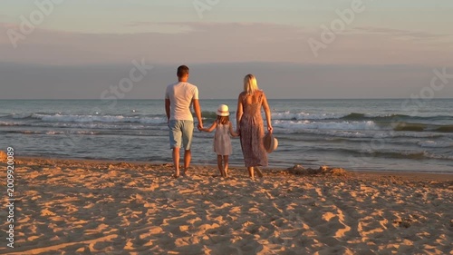 Back view of happy family walk on sand beach at sea at sunset. Mother father and little daughter outdoors by ocean. Summer vacation travel holiday