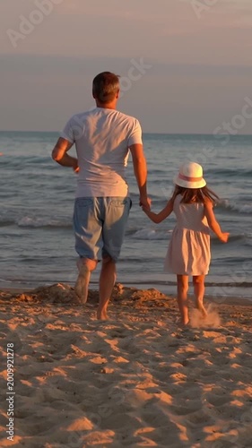 Father and little daughter run on sand beach to sea at sunset. Summer vacation travel holiday. Vertical shot
