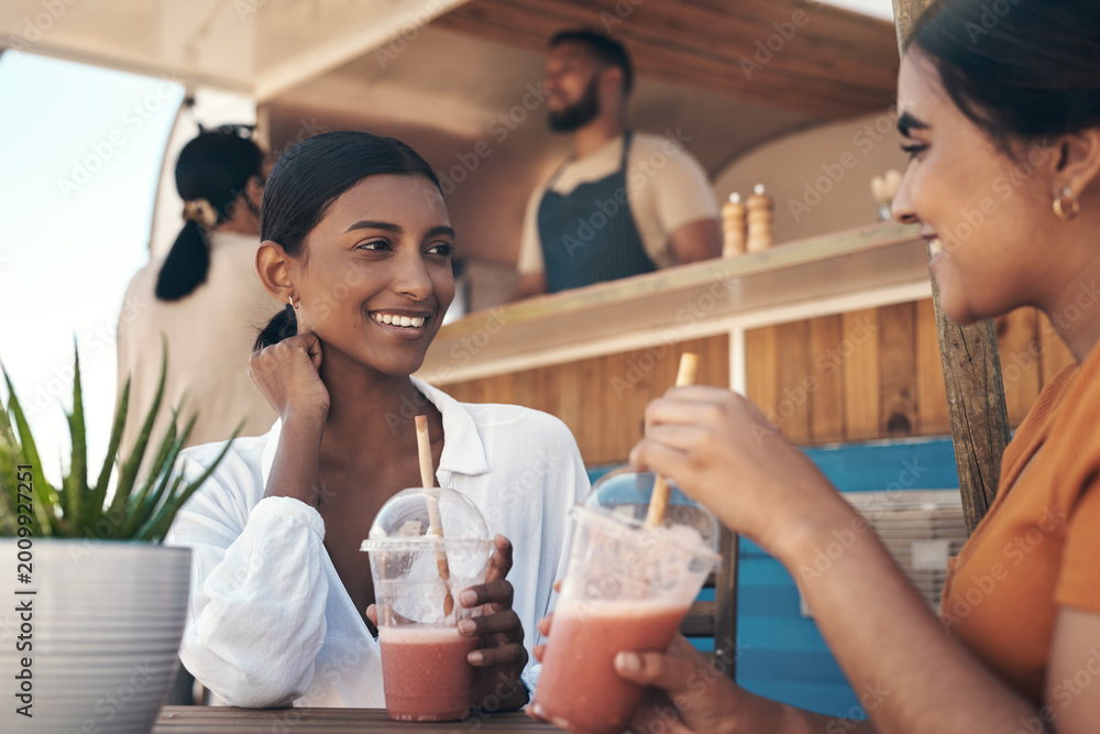 Fototapeta premium Friends, happy and smoothie outdoor by food truck for wellness, bonding or weekend break. Women, smile and talking for gossip, healthy drink or beverage as small business customer and hangout