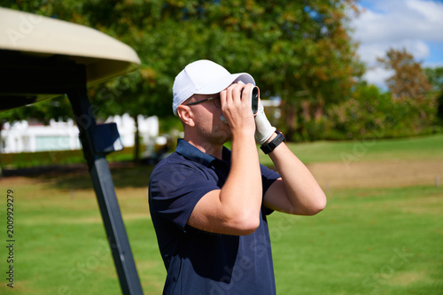 фотографія Man using rangefinder on golf course near golf cart.