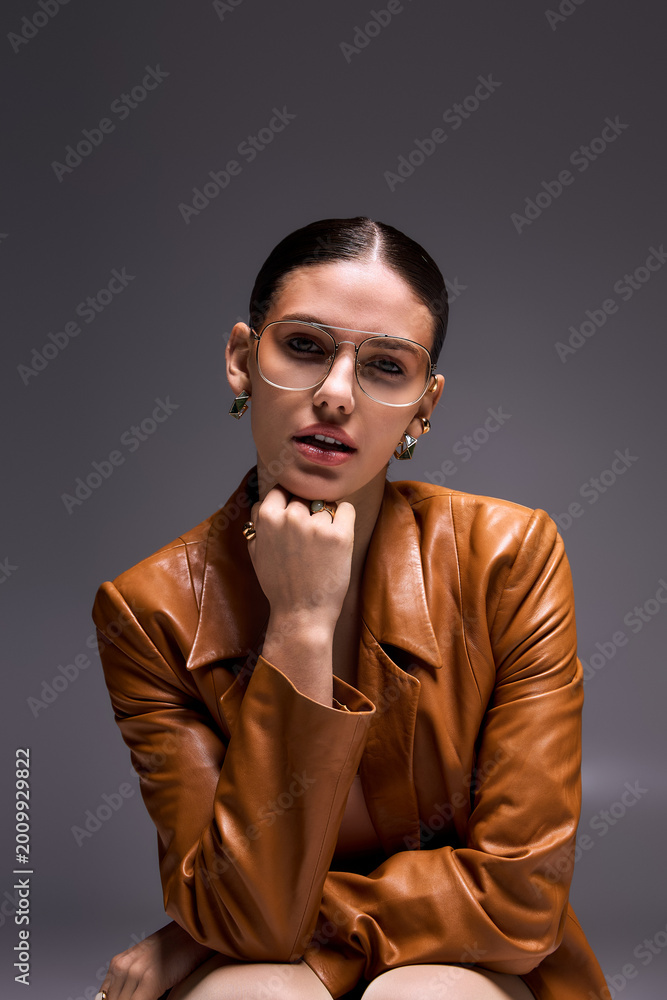 Obraz premium Stylish young woman exudes confidence in leather coat and glasses in studio setting
